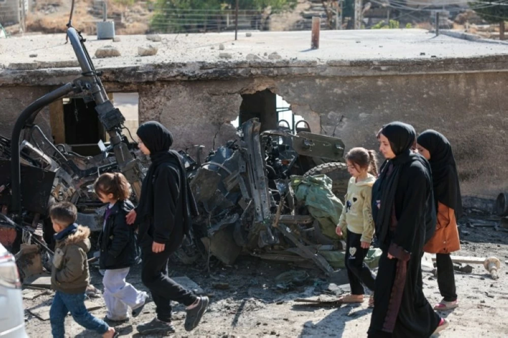 سوريون يمرون بجوار آلية عسكرية إسرائيلية مدمرة في بلدة بيت جن بريف دمشق. (إ ب أ)