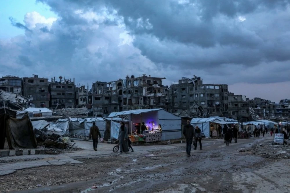 نازحون فلسطينيون يسيرون بين الملاجئ المؤقتة في حي الشيخ رضوان بغزة (إ ب أ)