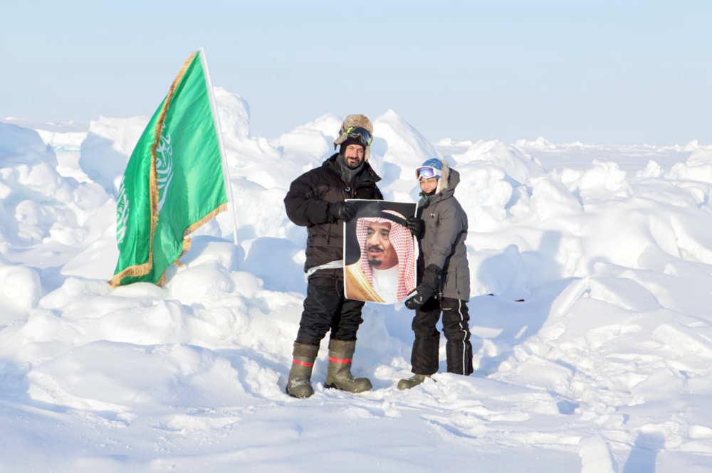 ريم فردوس وحسام شكري يرفعان صورة الملك سلمان في القطب الشمالي.  (عكاظ)