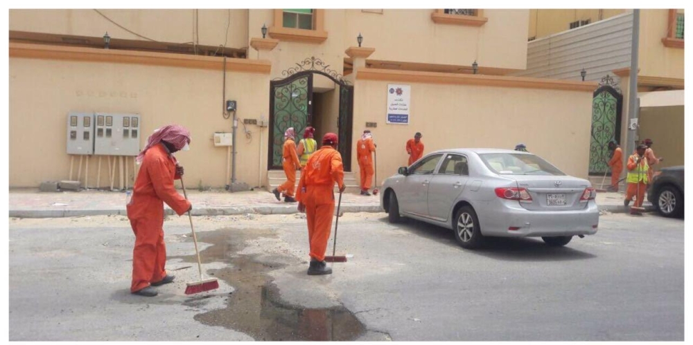 عمال نظافة خلال أداء أعمالهم بأحد الأحياء في الجبيل. (عكاظ)