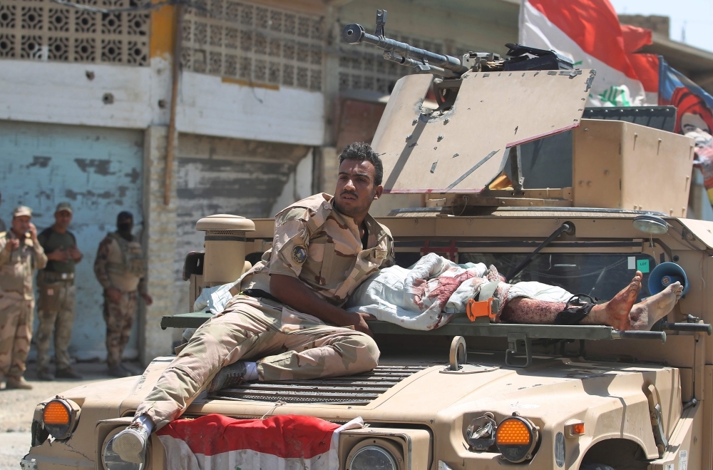 أحد أفراد القوات العراقية يجلس بجوار الضحية، الذي أصيب في هجوم انتحاري ( أ ف ب)
