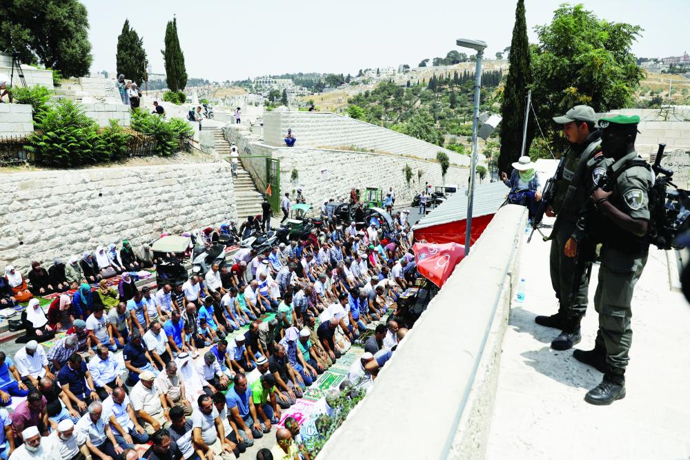 فلسطينيون يصلون في باب الأسباط في مدخل القدس القديمة، فيما جنديان إسرائيليان يراقبانهم أمس. (رويترز)