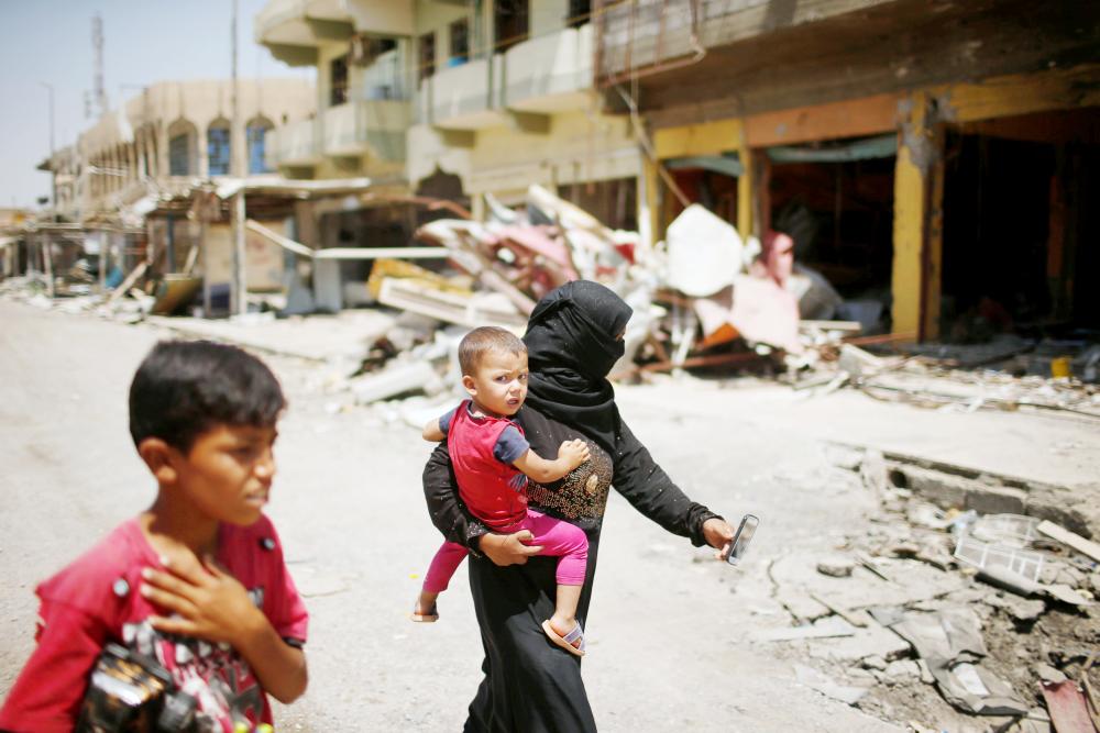 عراقية وطفليها يمشون في شارع بغرب الموصل حيث ركام المنازل المدمرة أمس. (رويترز)