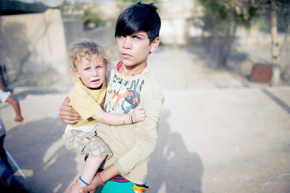 



طفل إيزيدي يحمل شقيقته في ملعب بسنجار أمس الأول، وفي الإطار لاجئات إيزيديات يبكين بحرقة خلال الاحتفال بالذكرى السنوية الثالثة للإبادة الجماعية الإيزيدية أمس. (رويترز)