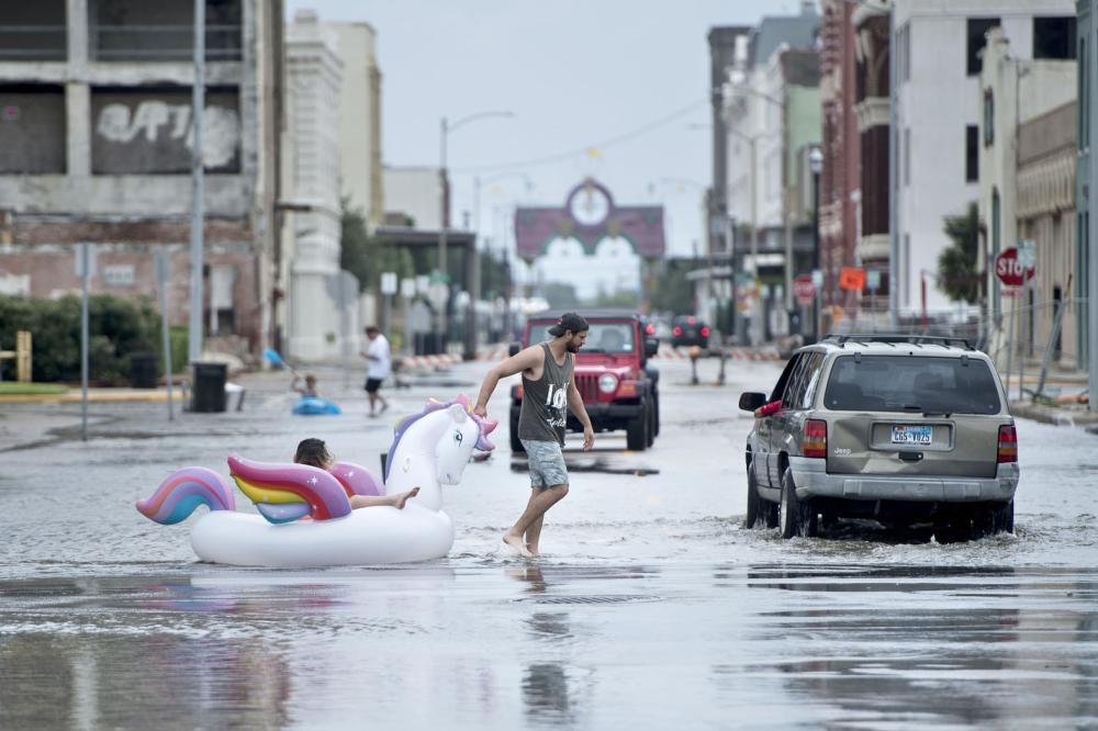 TOPSHOT - People make their way down partially flooded roads following the passage of Hurricane Harvey on August 26, 2017 in Galveston, Texas. / AFP / Brendan Smialowski
