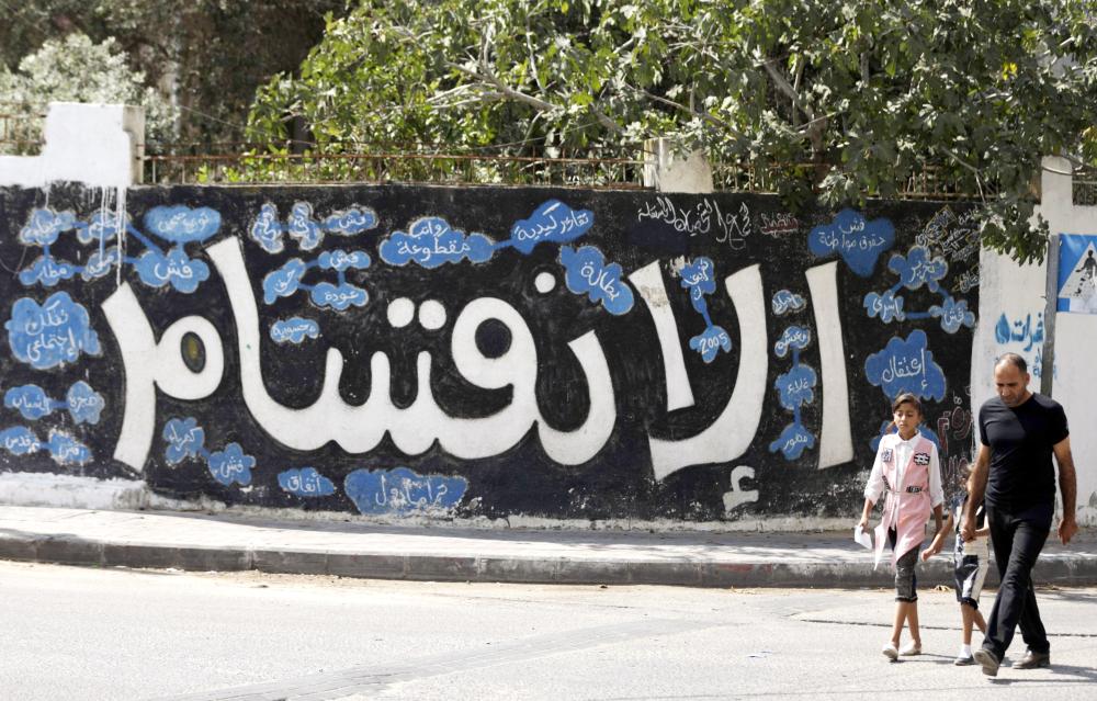 



 فلسطيني وابنته يمران أمام جدار مكتوب عليه «الانقسام» في غزة أمس. (‏أف ب) 
