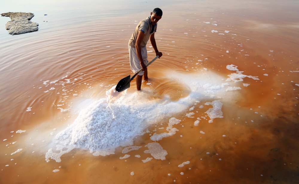 TOPSHOT - Iraqi salt workers harvest salt in saline water in the town of Diwaniyah, around 160 kilometres (100 miles) south of the capital Baghdad. The salt harvest season in Iraq lasts from April until October annually, as workers cultivate the marshes left by the rain, selling the salt by the bag for a sum of 5000 Iraqi dinars (equivalent to 4 US dollars), to be later sold to laboratories for crushing and purification. / AFP / Haidar HAMDANI
