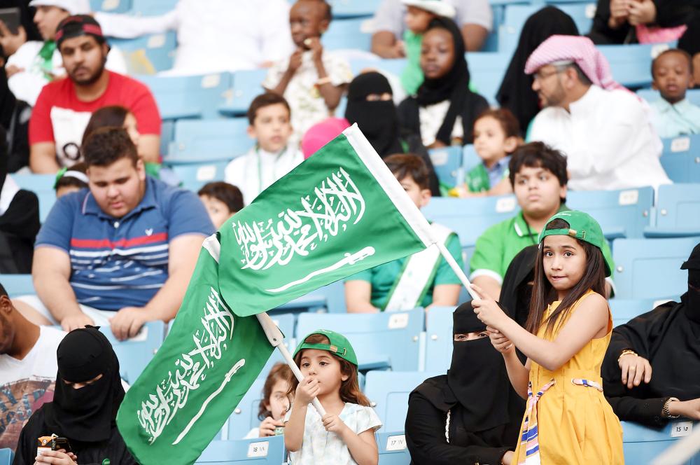 A Saudi girl waves a national flag as she stands by her seat in a stadium, attending an event in the capital Riyadh on September 23, 2017 commemorating the anniversary of the founding of the kingdom. The national day celebration coincides with a crucial time for Saudi Arabia, which is in a battle for regional influence with arch-rival Iran, bogged down in a controversial military intervention in neighbouring Yemen and at loggerheads with fellow US Gulf ally Qatar. / AFP / Fayez Nureldine
