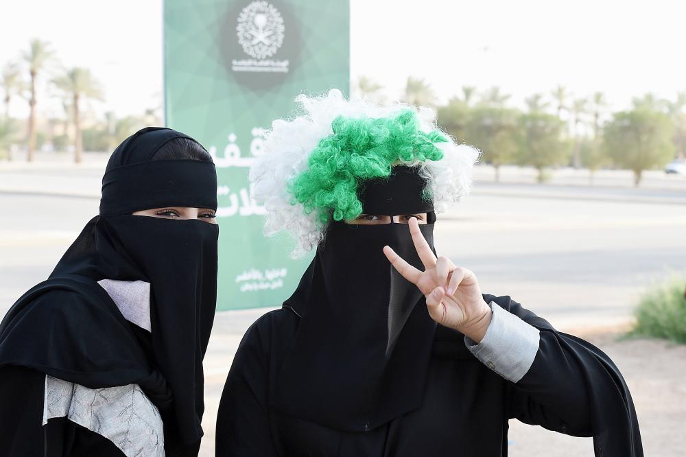 A Saudi woman flashes the victory gesture while wearing a coloured wig above her head-dress, as she arrives outside a stadium to attend an event in the capital Riyadh on September 23, 2017 commemorating the anniversary of the founding of the kingdom. The national day celebration coincides with a crucial time for Saudi Arabia, which is in a battle for regional influence with arch-rival Iran, bogged down in a controversial military intervention in neighbouring Yemen and at loggerheads with fellow US Gulf ally Qatar. / AFP / Fayez Nureldine
