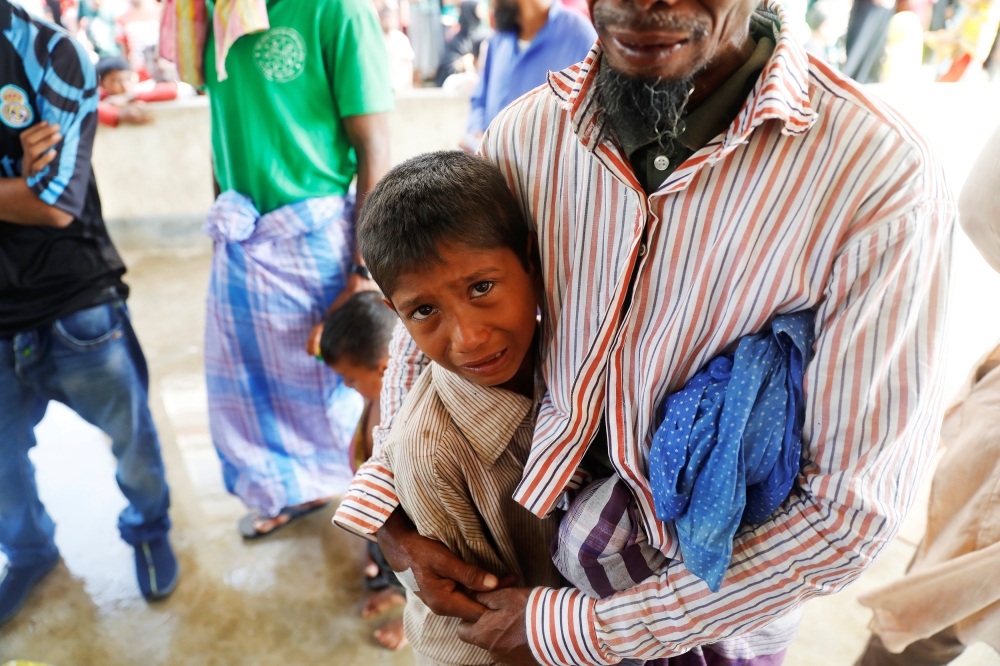 Lalu Miya hugs his surviving son as he cries over bodies of his wife and children, who died after a boat with Rohingya refugees capsized, as they were fleeing Myanmar, before their bodies were taken for the funeral just behind Inani Beach near Cox's Bazar, Bangladesh September 29, 2017. Miya, whose family was on the boat, just off the shore of Bangladesh, survived but three of his children and wife died in the accident. Two other of his children remain missing. REUTERS/Damir Sagolj