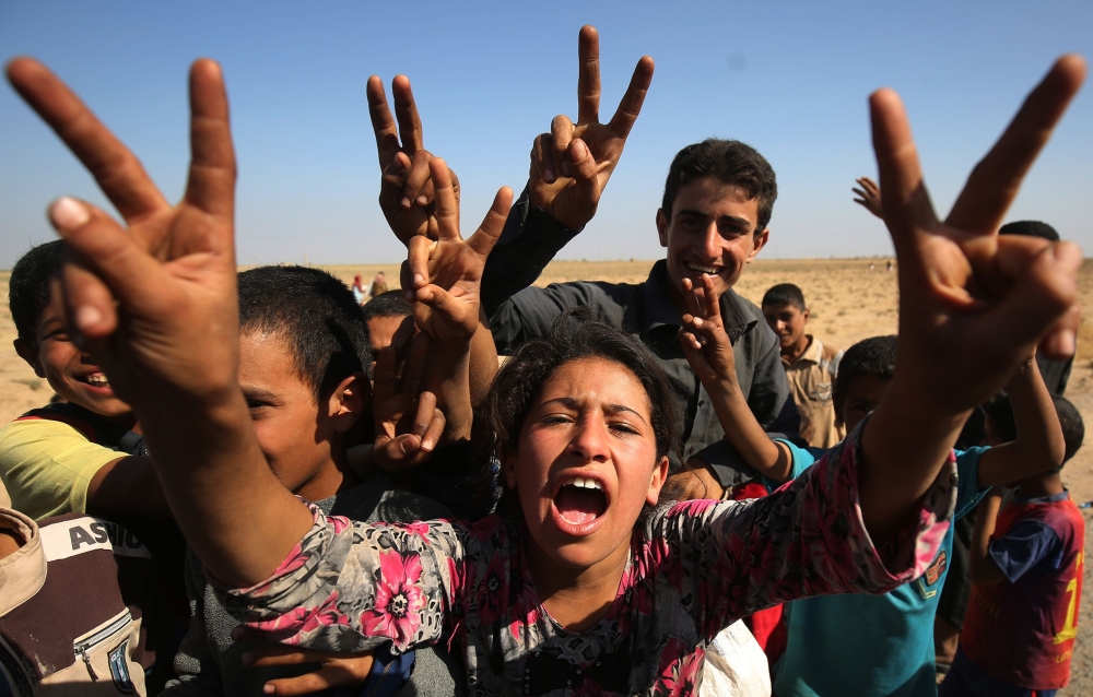 Iraqi children flash the victory sign as they receive food from a charity in a village on the outskirts of Hawija on October 6, 2017, a day after Iraqi forces retook the northern city from Islamic State (IS) group fighters. / AFP / AHMAD AL-RUBAYE 