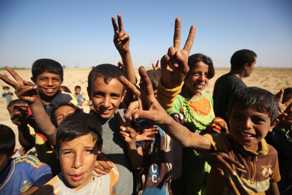 Iraqi children flash the victory sign as they receive food from a charity in a village on the outskirts of Hawija on October 6, 2017, a day after Iraqi forces retook the northern city from Islamic State (IS) group fighters. / AFP / AHMAD AL-RUBAYE 