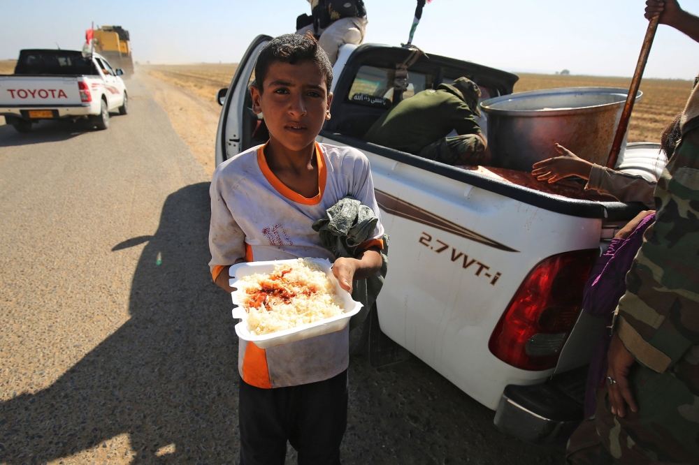 An Iraqi child receives food from a charity in a village on the outskirts of Hawija on October 6, 2017, a day after Iraqi forces retook the northern city from Islamic State (IS) group fighters. / AFP / AHMAD AL-RUBAYE 