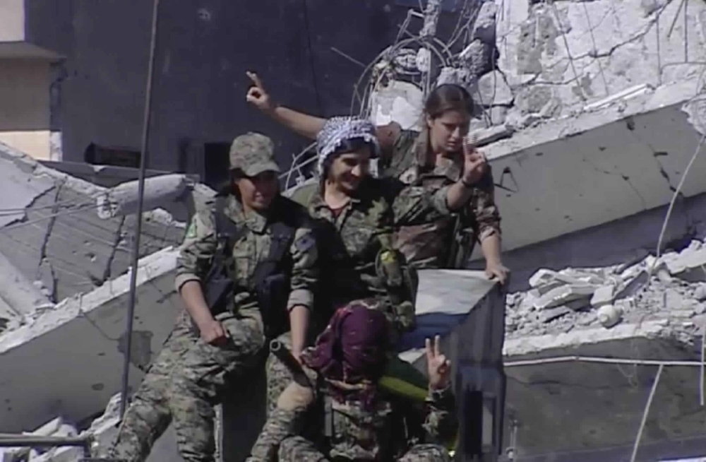 This frame grab from a video released on Thursday, Oct. 19, 2017 provided by Ronahi TV, a Kurdish TV channel media outlet that is consistent with independent AP reporting, shows members of a Kurdish female militia, the Women's Protection Units, flashing victory signs as they celebrate the victory against the Islamic State group, in Raqqa, Syria. The militia that took part in freeing the northern Syrian city of Raqqa from the Islamic State group said it will continue the fight to liberate women living under the extremist group's brutal rule. (Ronahi TV, via AP)