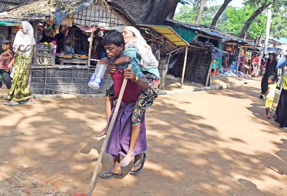 نازح روهينغي يحمل إمرأة مسنة على ظهره متوجهاً إلى مخيم أقامته بنغلاديش للنازحين قرب الحدود مع ميانمار. (رويترز)