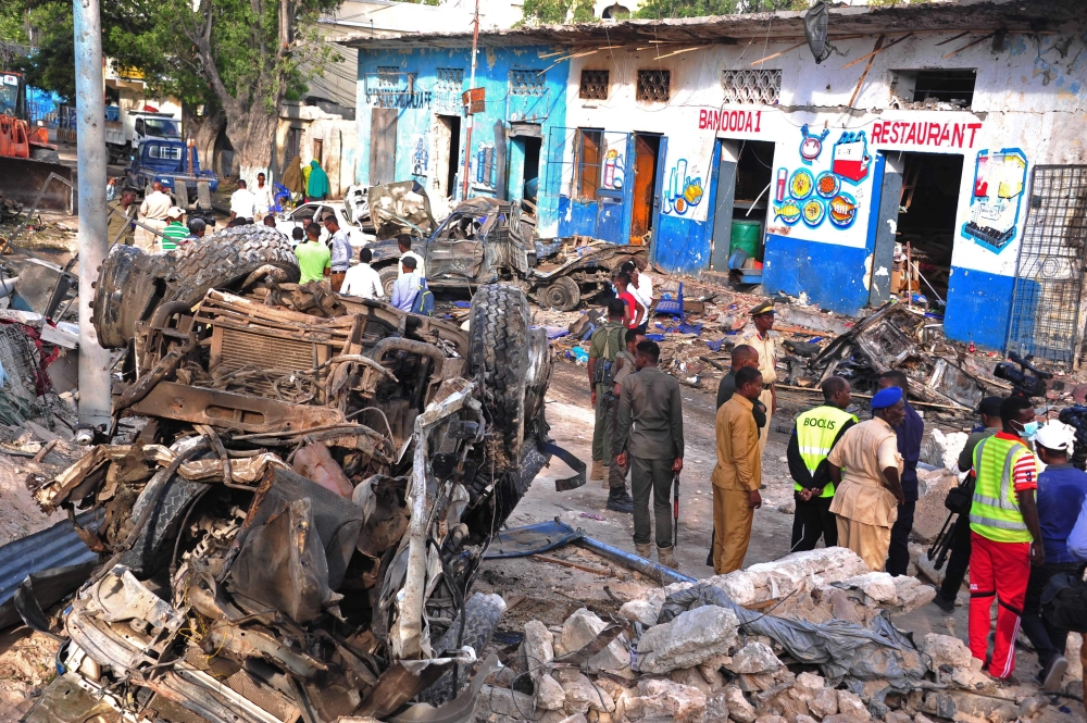 Somali security forces and civilians walk among damages at the scene of a blast on October 29, 2017, a day after two car bombs exploded in Mogadishu. Somalia's security ministry said today that forces had killed two gunmen and captured three after a siege at a Mogadishu hotel following a twin car bombing that left at least 14 dead. The attack began when a car bomb exploded outside the hotel entrance, followed by a minibus loaded with explosives going off at a nearby intersection. / AFP / Mohamed ABDIWAHAB 