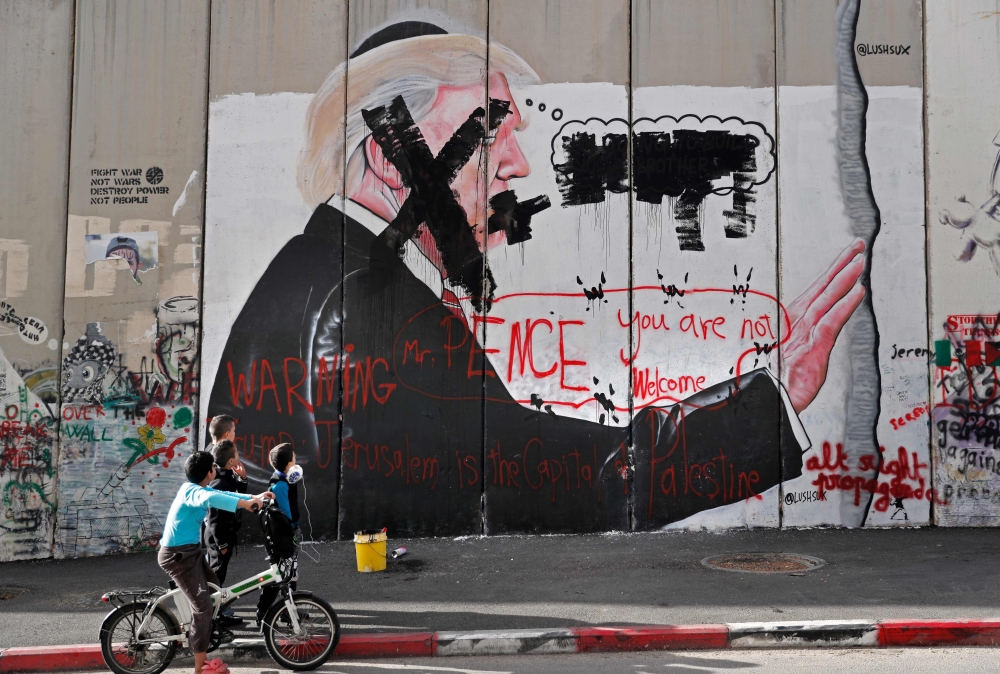 Palestinian children look at vandalised graffiti depicting US President Donald Trump and slogans against US Vice President Mike Pence painted on Israel's controversial separation barrier in the West Bank city of Bethlehem during clashes with Palestinian protestors near an Israeli checkpoint on December 7, 2017. US President Donald Trump's recognition of Jerusalem as Israel's capital may bring little immediate concrete change but risks sparking another round of violence in a conflict that has lasted decades. / AFP / THOMAS COEX
