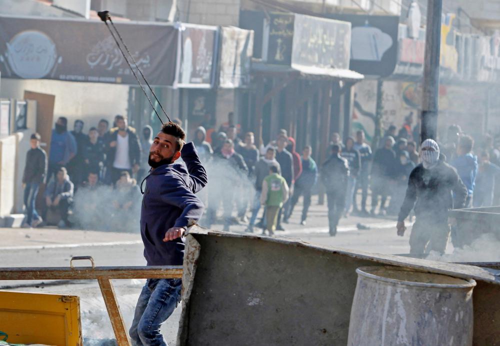 A Palestinian protestor throws stones towards Israeli forces during clashes near an Israeli checkpoint in the West Bank town of Bethlehem on December 8, 2017.  Palestinians clashed with Israeli security forces after calls for a 