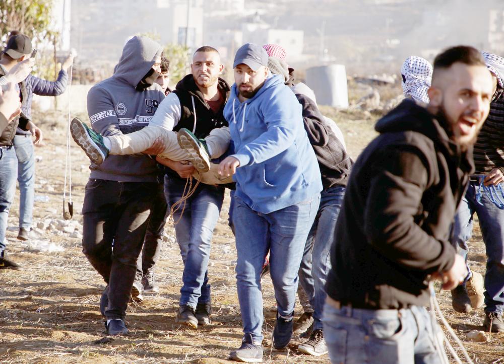 Palestinian protesters carry a wounded comrade during clashes with Israeli troops near an Israeli checkpoint in the West Bank city of Ramallah on December 8, 2017. Israel deployed hundreds of additional police officers following Palestinian calls for protests after the main weekly Muslim prayers against US President Donald Trump's recognition of Jerusalem as Israel's capital. / AFP / ABBAS MOMANI

