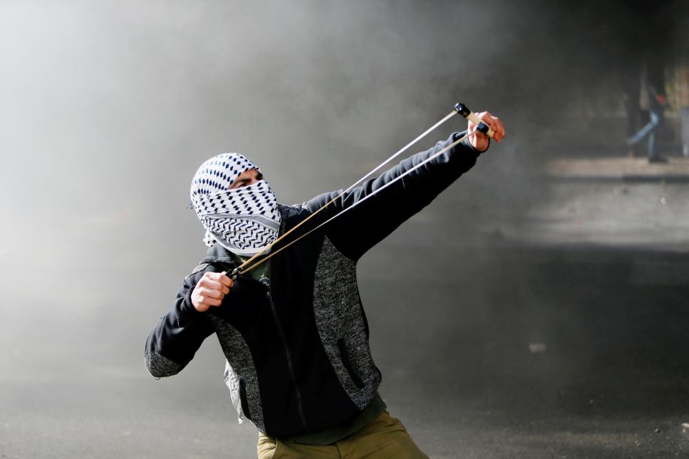 A Palestinian protester uses a sling shot to hurl stones towards Israeli troops during clashes as Palestinians call for a 