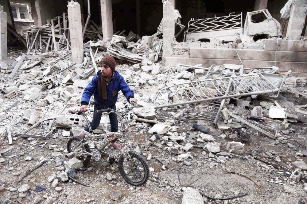 TOPSHOT - A Syrian boy walks with a bike amid the rubble following reported bombardment by Syrian and Russian forces in the rebel-held town of Hamouria, in the Eastern Ghouta, on January 6, 2018. Regime and Russian air strikes on a rebel-held enclave near the Syrian capital killed at least 17 civilians, a war monitor said. / AFP / ABDULMONAM EASSA
