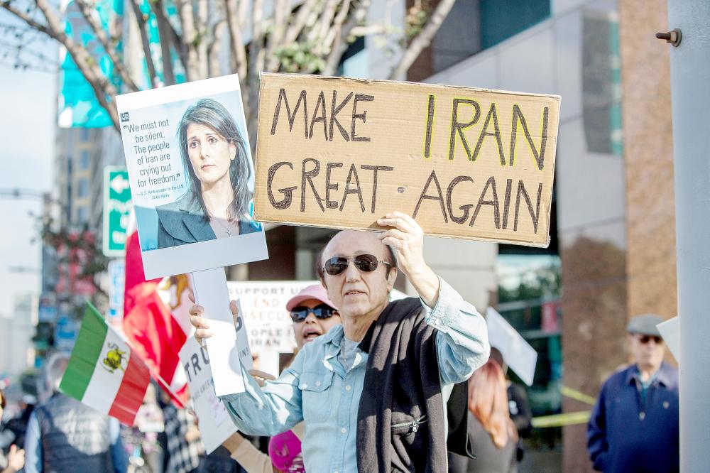 إيراني يرفع لافتة كتب عليها «لنعيد عظمة إيران»، وصورة مندوبة واشنطن نيكي هيلي،  خلال وقفة لدعم الانتفاضة في لوس أنجلوس أمس الأول. (رويترز)
