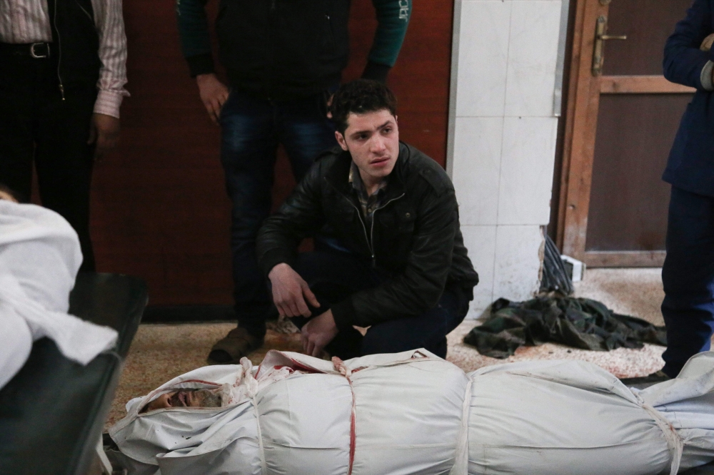 A Syrian man reacts next to the body of a victim at a makeshift hospital following reported artillery shelling in Hammuriyeh in the rebel-held Eastern Ghouta area, on the outskirts of the capital Damascus, on January 12, 2018.  / AFP / ABDULMONAM EASSA
