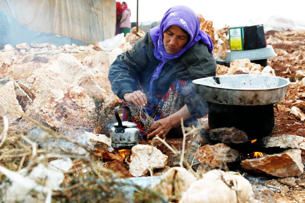 A Syrian woman, who fled from the outskirts of southern Idlib due to conflict between government forces and opposition fighters, cooks over a fire at the make-shift camp of Kalbeed near the Bab al-Hawa crossing on the Syria-Turkey border on January 17, 2018. / AFP / Zein Al RIFAI
