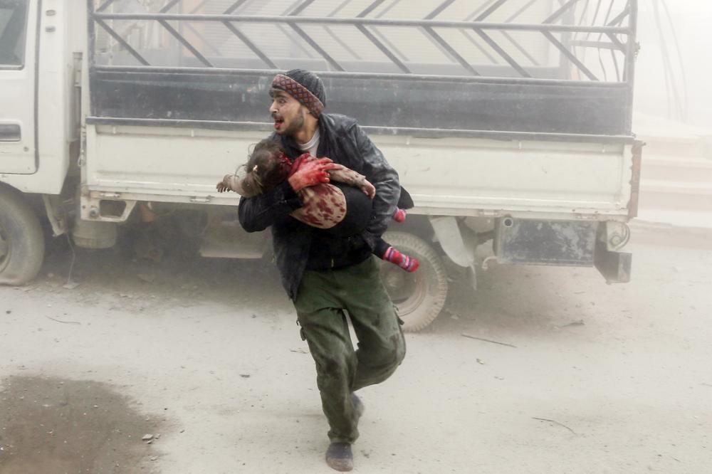 A man carries a child as he flees from reported Syrian air force strikes that hit the rebel-held town of Saqba, in the besieged Eastern Ghouta region on the outskirts of the capital Damascus, on February 6, 2018. Fresh regime strikes on a besieged rebel-held enclave near Damascus killed more than 60 civilians on February 6, despite mounting Western pressure on Syrian President Bashar al-Assad. / AFP / ABDULMONAM EASSA
