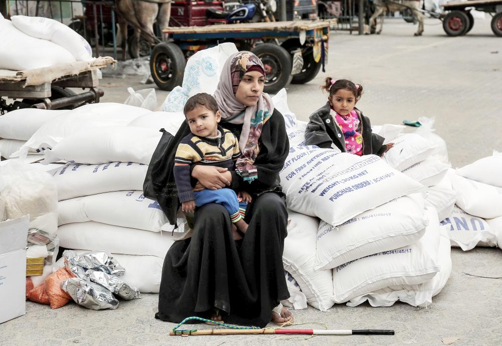 



 فلسطينية تجلس مع طفليها بعد تلقي مساعدات غذائية من «الأونروا» في مخيم خان يونس للاجئين جنوب غزة أمس. (أ.ف.ب)