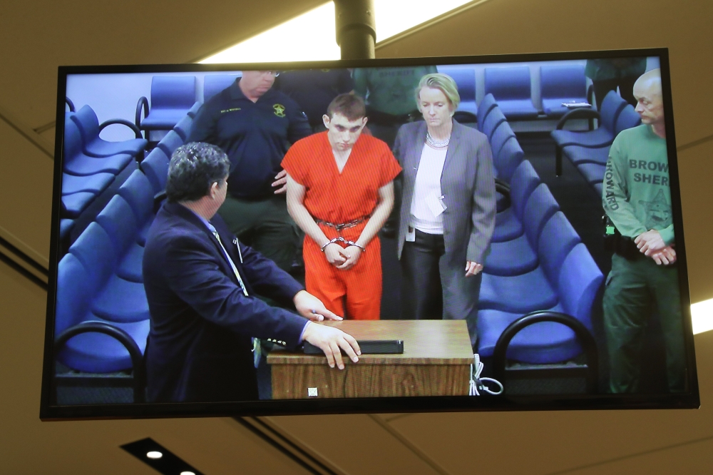 TOPSHOT - Hector Romero Asst. Public Defender(L) and Melisa McNeill, Public Defender (R) are seen on screen at the first appearance court for high school shooting suspect Nikolas Cruz(C) on February 15, 2018 at Broward County Court House in Fort Lauderdale, Florida. The heavily armed teenager who gunned down students and adults at a Florida high school was charged Thursday with 17 counts of premeditated murder, court documents showed. Nikolas Cruz, 19, killed fifteen people in a hail of gunfire at Marjory Stoneman Douglas High School in Parkland, Florida. Two others died of their wounds later in hospital, the sheriff's office said.
 - 
 / AFP / POOL / Susan STOCKER
