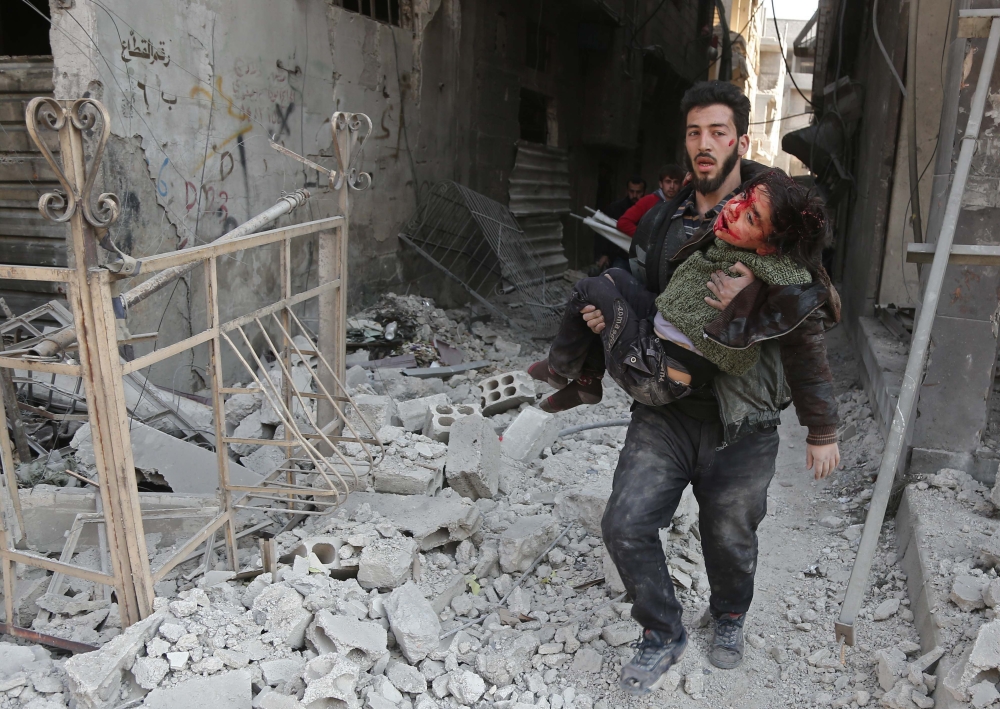 EDITORS NOTE: Graphic content / A Syrian man rescues a child following a reported regime air strike in the rebel-held town of Hamouria, in the besieged Eastern Ghouta region on the outskirts of the capital Damascus on February 21, 2018. Ten civilians were killed today in fresh air strikes by the Syrian regime on rebel-held Eastern Ghouta, where 270 people have died in three days of bombardment, a monitor said. / AFP / ABDULMONAM EASSA 
