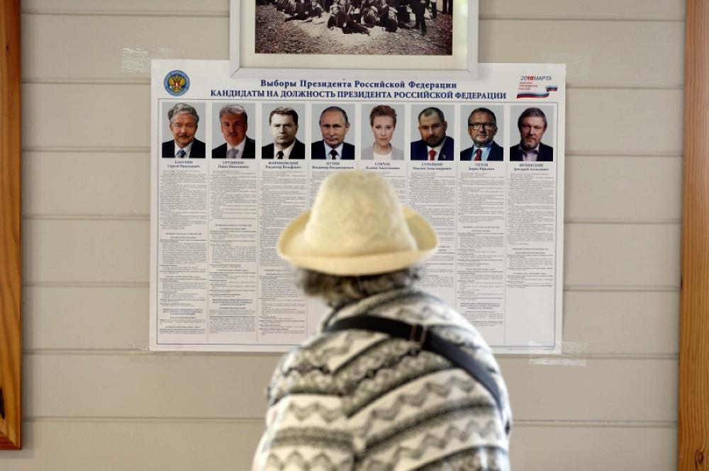 رجل روسي يطالع منشورا لمرشحي الرئاسة الروسية. (أ.ف.ب)