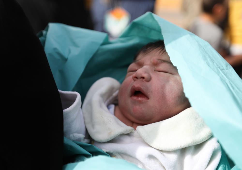A new-born that was delivered on the way as Syrians were evacuated from the rebel-held town of Harasta in Eastern Ghouta is held by a woman upon their arrival at a camp for displaced people in Maaret al-Ikhwan, in Syria's rebel-held Idlib province on March 23, 2018. Hundreds of fighters evacuated by the Syrian regime from their Eastern Ghouta bastion arrived in Idlib province, the Britain-based Syrian Observatory for Human Rights said. / AFP / OMAR HAJ KADOUR
