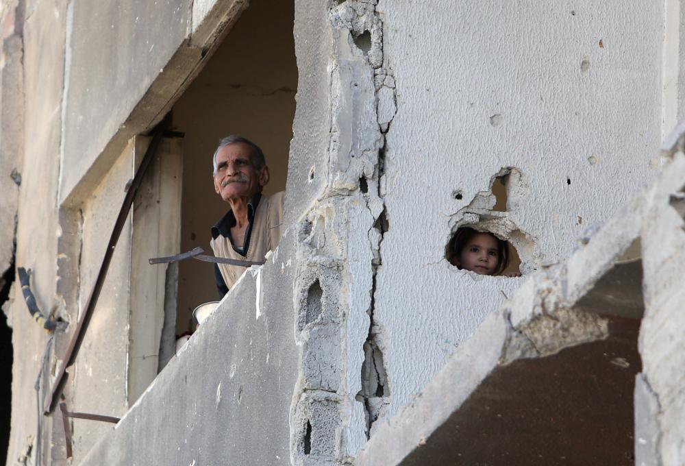 



طفلة سورية تطل من فتحة في جدار مدمر في منزل أسرتها بدوما أمس الأول. (رويترز)