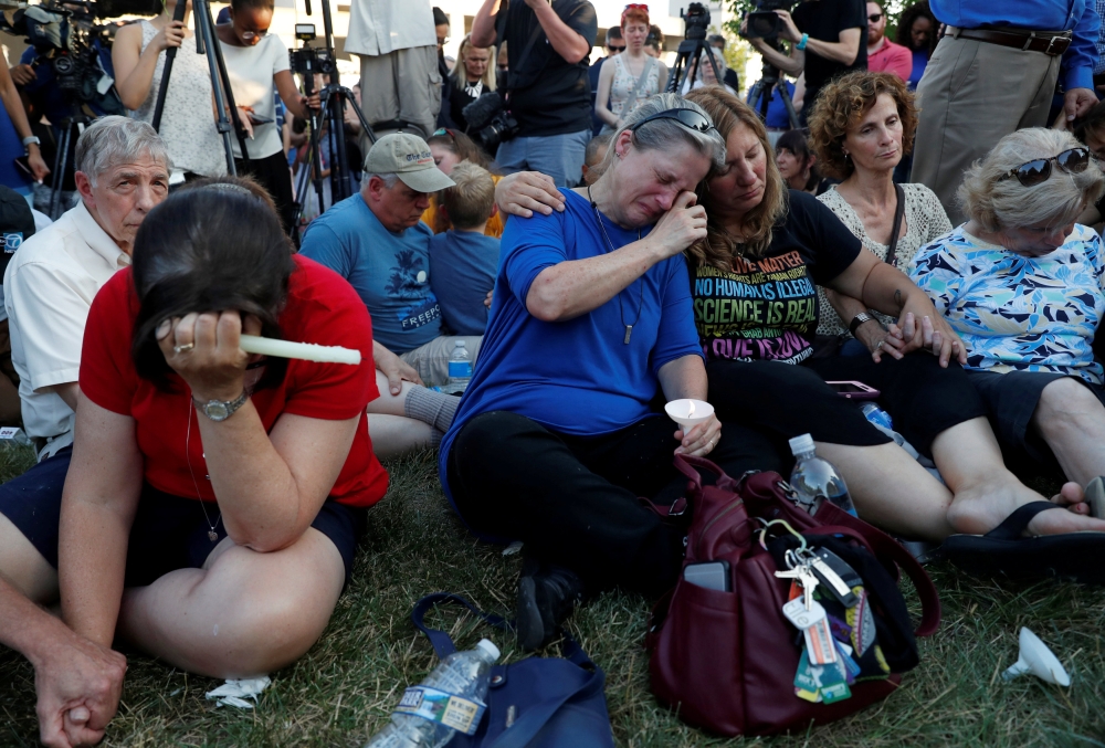 Community members Carol Geithner, center left, and Yasemine Jamison take part in a candlelight vigil with Una Cooper, (L) and others near the Capital Gazette, the day after a gunman killed five people inside the newspaper's building in Annapolis, Maryland, U.S., June 29, 2018. REUTERS/Leah Millis