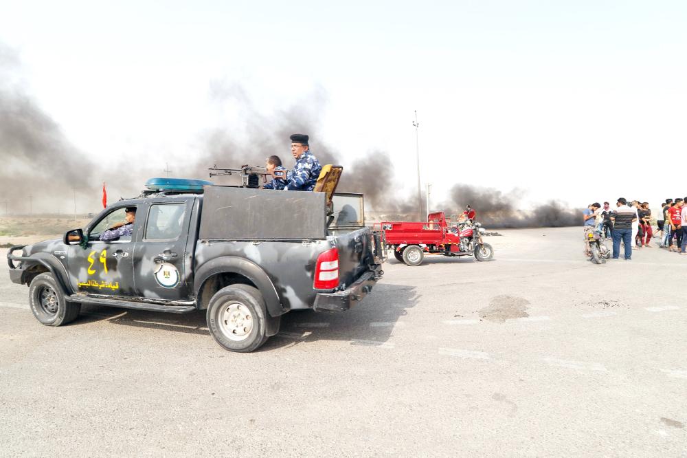 Iraqi police drive past protestors during a gathering northwest of the southern city Basra on July 17, 2018, during a demonstration against unemployment and a lack of basic services.  / AFP / Haidar MOHAMMED ALI
