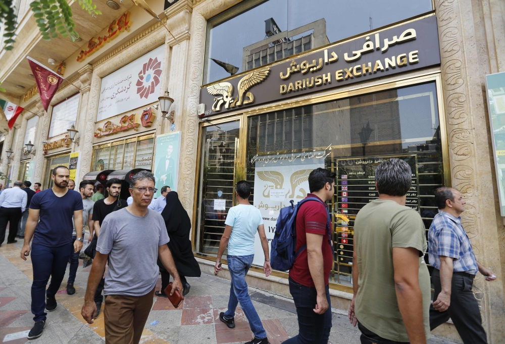 People walk in front of a currency exchange shop in the Iranian capital Tehran on August 8, 2018.  US President Donald Trump warned the world the previous day against doing business with Iran as Washington reimposed 