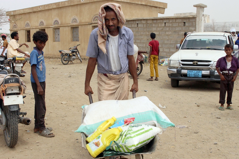 This picture taken on August 15, 2018 shows a displaced Yemeni man from Hodeida carrying food aid from a Japanese NGO in a barrow, in the northern district of Abs, in Hajjah province. / AFP / ESSA AHMED
