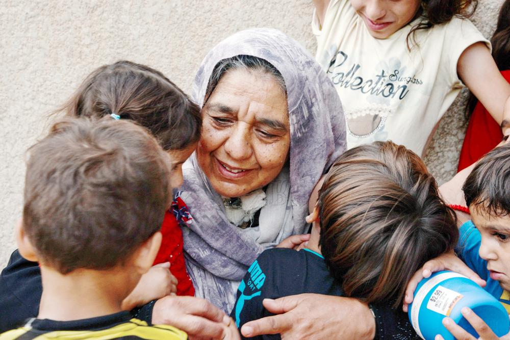 Sana Ibrahim (C), a 61-year-old Iraqi matriarch and caretaker for 22 grandchildren, embraces her family members in a courtyard in their home in the northern city of Mosul on August 14, 2018. Despite the Islamic State group being driven from Mosul, 61-year-old Sana Ibrahim faces daily hardship in looking after her 22 grandchildren and her Alzheimer's-ridden septuagenarian husband, after losing her four sons and son-in-law to the jihadists during their occupation. / AFP / Zaid AL-OBEIDI
