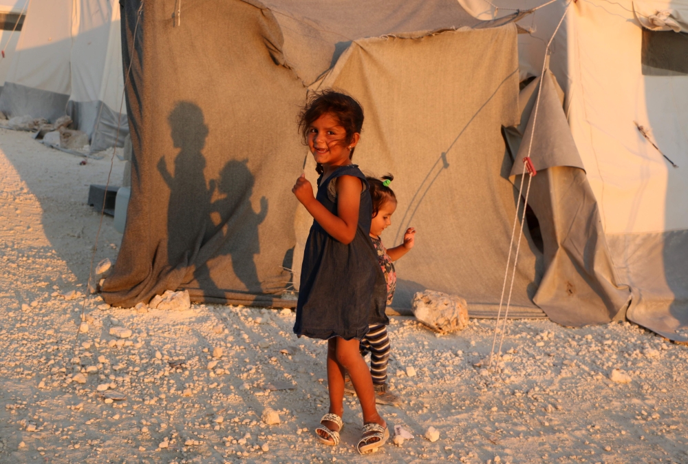 TOPSHOT - Displaced Syrian girls stand next to a tent provided by a Turkish humanitarian organisation at a camp for displaced people in the northern Idlib province on August 29, 2018. UN Secretary-General Antonio Guterres warned today that full-scale military operations in Syria's Idlib province could lead to a 