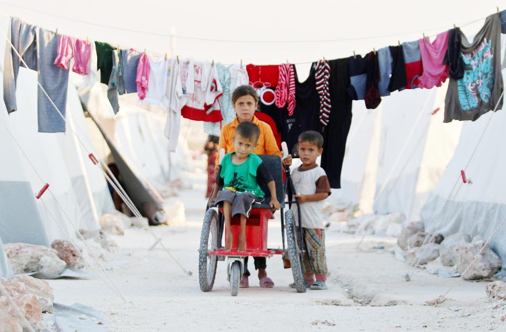 



أطفال سوريون يدفعون معوقا على كرسي متحرك في مخيم للنازحين في إدلب أمس الأول.  (أ. ف. ب)