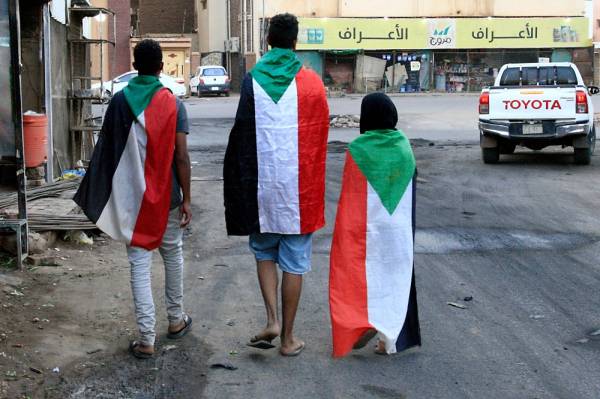 Sudanese demonstraters wear their national flag as they celebrate in Khartoum early on August 3, 2019, after Sudan's ruling generals and protest leaders reached a «full agreement» on the constitutional declaration. The document is complementary to a power-sharing deal signed on July 17 that aims to form a joint civilian-military ruling body which will oversee the formation of a transitional civilian government and parliament to govern for a three-year transition period. / AFP / Ebrahim HAMID
