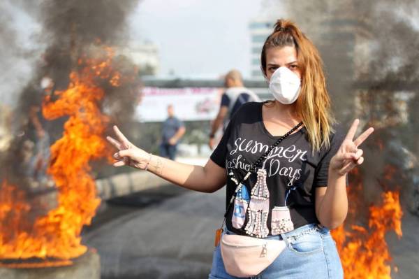



لبنانية ترفع علامة النصر أمام إطارات محترقة خلال مظاهرة حاشدة في الضواحي الشمالية لبيروت أمس الأول. (أ.ف.ب)