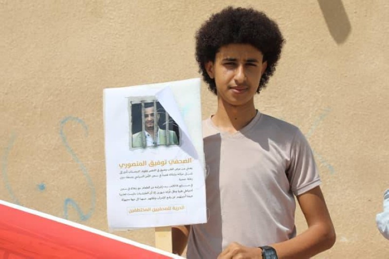صحفي يحمل صورة زميله في احتجاجات مأرب (عكاظ)