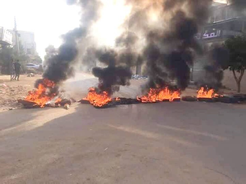 



 سودانيون يرفعون علم بلادهم أمام إطارات محترقة في أحد شوارع الخرطوم.