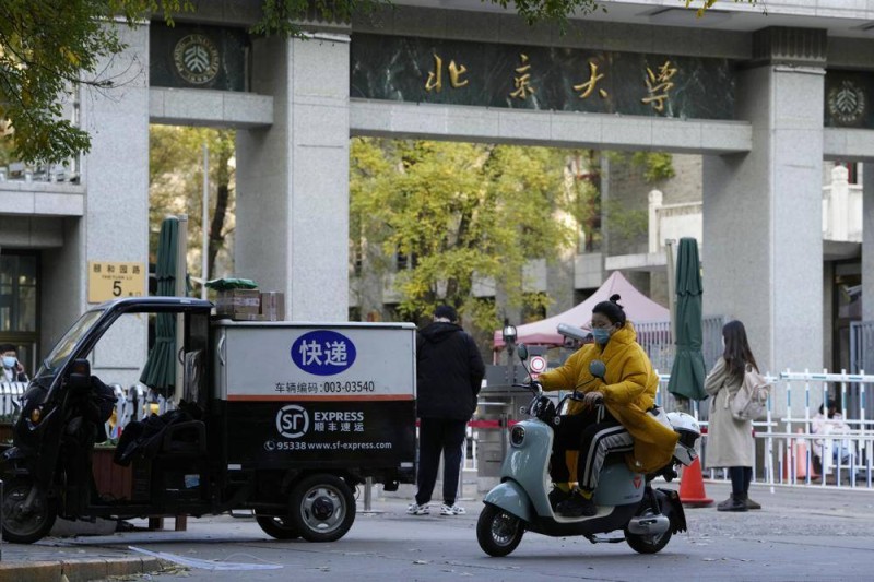امرأة ترتدي الكمامة أثناء قيادتها دراجتها النارية أمام بوابة جامعة بكين. (وكالات)