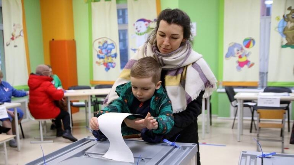 طفلٌ يضع صوت والدته في صندوق الاقتراع بالانتخابات الرئاسية الروسية - مدينة بطرسبورع.